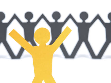 A yellow paper figure raising his arms. A paper man chain against the white background. Selective focus on the foreground.の写真素材