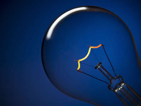 Close up on a turned on light bulb over a blue background.の写真素材