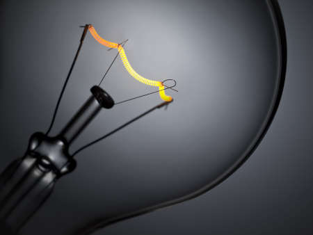 Close up on a turned on light bulb over a grey background.の写真素材