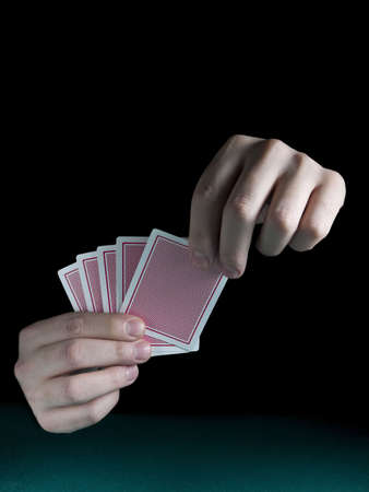 A man's hand holding five cards over a green felt.
