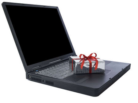 Small gift wrapped with a red ribbon over a black laptop isolated on white. Black copy space on screen.の写真素材