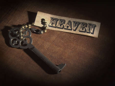 An old key attached to a label saying HEAVEN over a wooden table.の写真素材