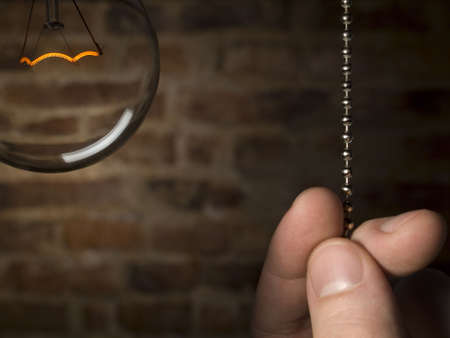 A man's hand is about to switch off the bulb light. Brick wall as background.の写真素材