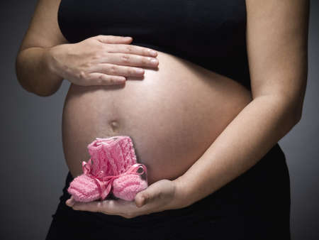 Pregnant woman holding a pair of pink baby booties.
