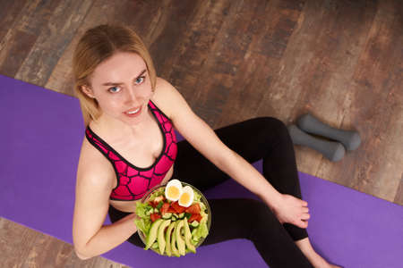 Young woman eating a healthy lunch and sitting on a yoga mat