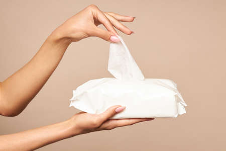 Hygiene. Female hands takes wet wipes from white packaging on a beige background. Daily hygiene for...