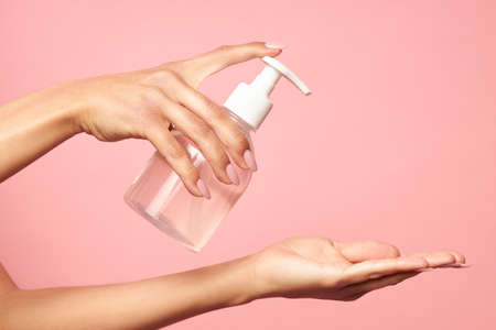 Hand hygiene. Woman applying disinfectant on her palm on a pink background. High quality photo