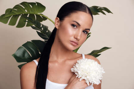 Womans face Flower behind the model. Beautiful girl with a flower on a beige background and...
