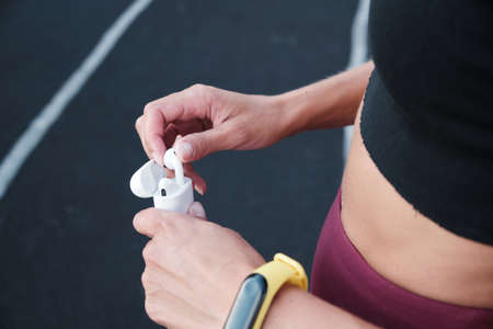Close up of the hands of a young girl in sportswear in a Park taking wireless headphones out of the...