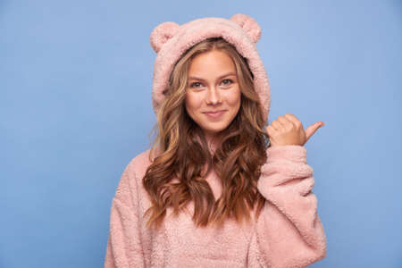 Close-up portrait of a pretty attractive cheerful girl pointing her fingers ad advertising advice decision to copy space in pink clothes bear on a blue backgroundの写真素材