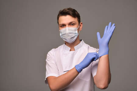 Young doctor wearing blue gloves on gray backgroundの写真素材