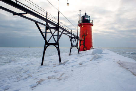 Red lighthouse during sunset with ice and snowの写真素材