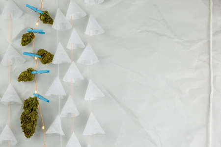 Nuggets of weed pinned to lights with paper on strings againts textured background