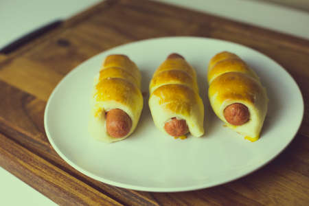 Pigs in a blanket on white plate set on wood cutting boardの写真素材