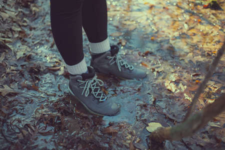 female hiker with boots in leafy puddle in spring during sunsetの写真素材
