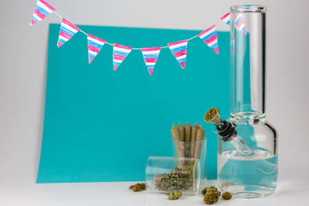 Glass bong with weed buds and cone joints in glass jars with festive red, white and blue pennants against blue and white backdropの写真素材