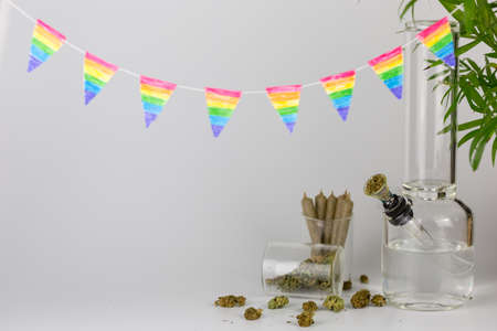 Bong with tropical plant, cone joints, weed buds in glass jar and rainbow pennants against a white backdropの写真素材