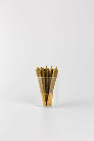 Five brown, cone shaped joints in glass jar isolated on whiteの写真素材