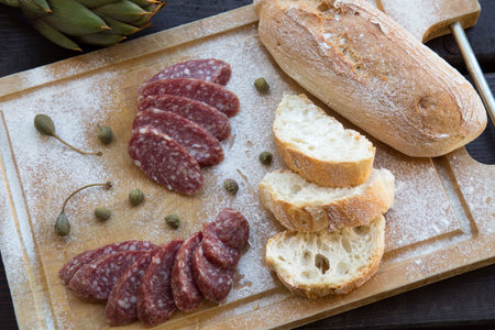 sliced bread with salami and artichoke on wooden boardの写真素材
