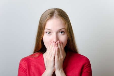 Beautiful woman in a red jacket covering her mouth with hands.の写真素材