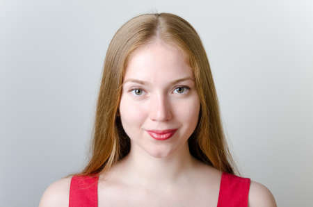 Beautiful blonde woman with long hair dressed in red on grey background.の写真素材
