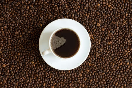 Cup of coffee on a coffee beans background. Focus on coffee with bubbles.