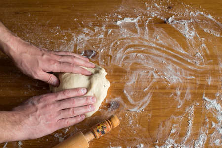 Hands of a man making batter on a wooden table.