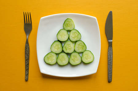 A plate with sliced cucumber, fork and knife on yellow background.の写真素材