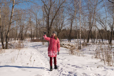 Woman in pink taking pictures with a little point-and-shoot camera in a winter forest.の写真素材