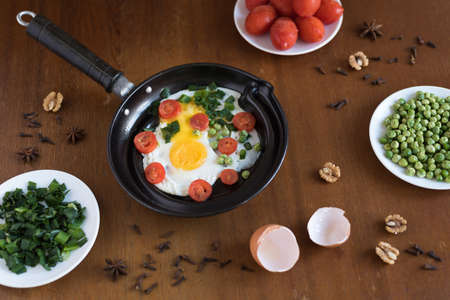 Fried eggs with tomatoes, green peas and spring onions