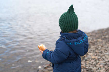 Child with a piece of bread on a river bankの写真素材