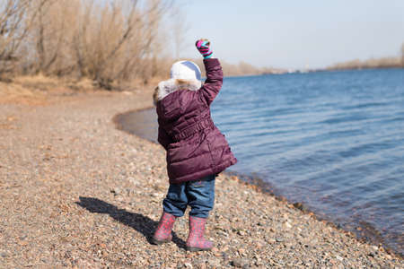 Little girl throwing stones into river in spring