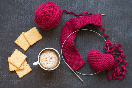 Knitting with red yarn and needles, heart, a cup of coffee and five crackers on dark grunge boardの写真素材