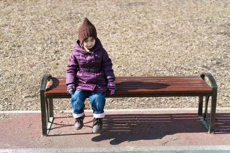 Little girl sitting of a bench in the parkの写真素材