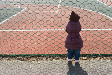 Little girl staring at a field throw the metal meshの写真素材