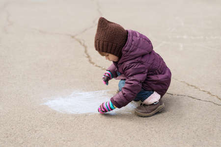 Little girl drawing with a piece of chalk on asphaltの写真素材
