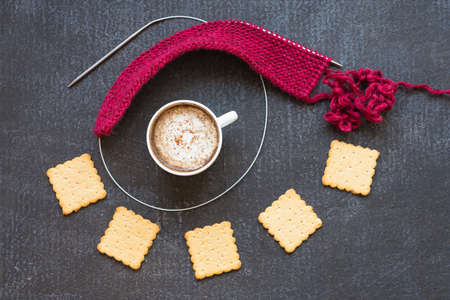 Knitting with red yarn and needles, a cup of coffee and crackers on a dark painted grunge background.の写真素材