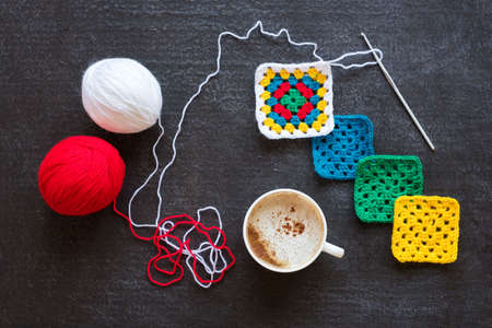 Balls of yarn, crocheted motives and a cup of coffee on grunge black background.の写真素材