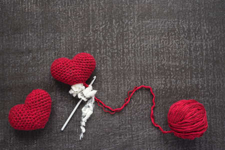 Crocheted red hearts on a grunge board with a ball of woolen yarn. One heart is not finished.の写真素材