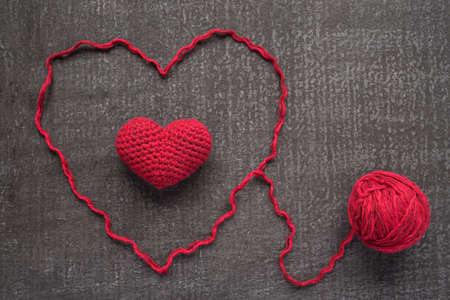 Crocheted red heart on a grunge board with a ball of woolen yarn.の写真素材