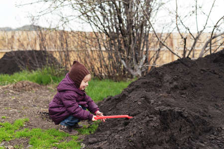 Little girl with a red shovel working in a spring garden.の写真素材