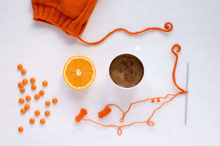 Cup of coffee, orange, candies and a handmade hat on white backgroundの写真素材