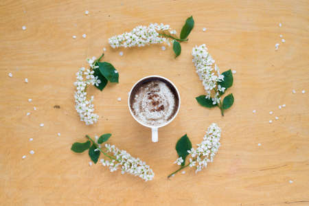 Coffee and twigs of blooming bird cherry laying out in circle on wooden board.の写真素材