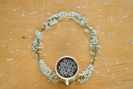 Coffee and twigs of blooming bird cherry laying out in circle on wooden board.の写真素材
