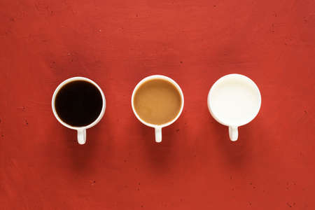 Three cups with coffee and milk on a red painted board.の写真素材