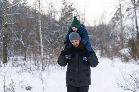 Father and child walking in a winter forest. The child is sitting on fathers' shoulders.の写真素材
