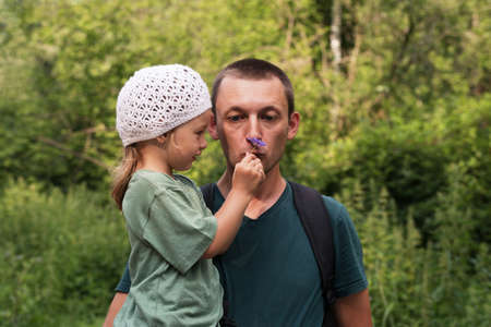Father and daughter in the summer forest. He is holding her. She is giving him a little flower to smell.の写真素材