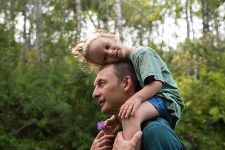 Little girl sitting on her father's shoulders in a summer forest.の写真素材