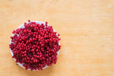 Red berries of viburnum on a plate on a woodden background.の写真素材
