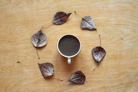 Cup of coffee and dried autumn leaves placed in a circle on a wooden background. Shot from above.の写真素材